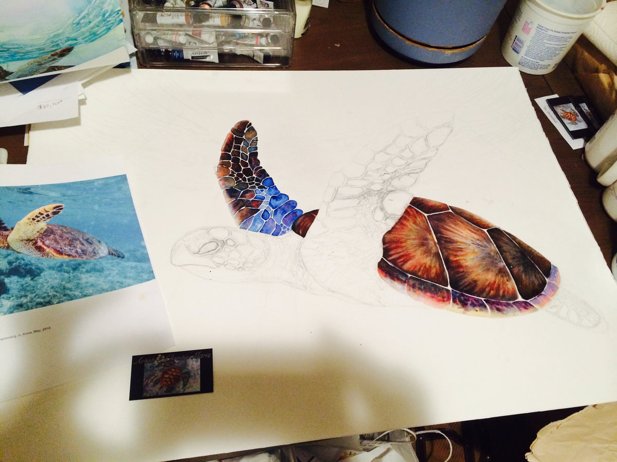 Aloha Spirit watercolor in progress showing layered transparent glazing a partially completed sea turtle drawing, with color reference photos of a sea turtle placed nearby.  Artist Christie's workspace with art supplies on art table.