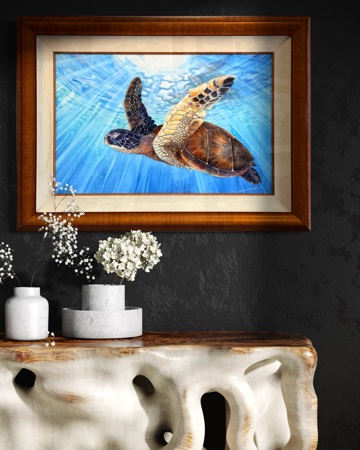 Aloha Spirit , Framed artwork by Christie Marie Elder of a sea turtle swimming underwater on a dark wall above a decorative table.